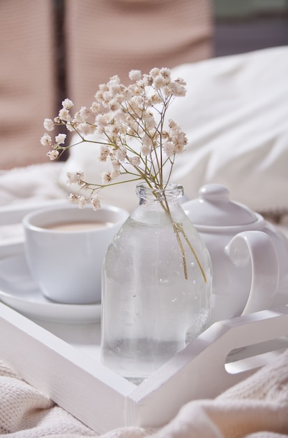 Close up of cup of tea, milk, teapot and bouquet of white flowers on the white tray.