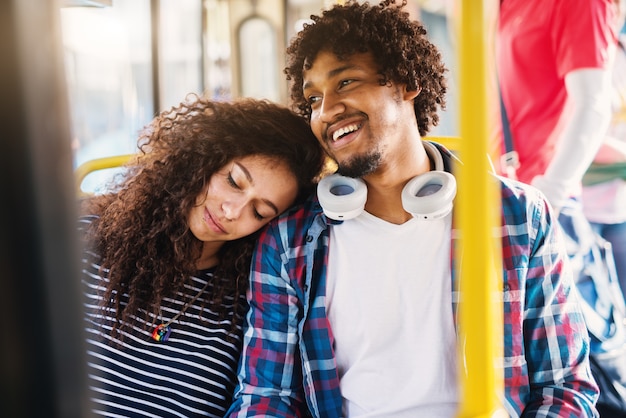 Close up of a cute tired curly girl leaning her head on her boyfriends shoulder while sitting in a bus.