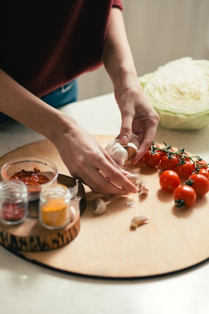 Close up of the cutting board with tomatoes and spices. Woman holding cloves of garlic