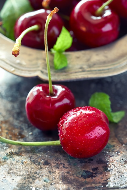 Close up on dark cherries and fresh mint leaves in pewt bowl on grunge metal