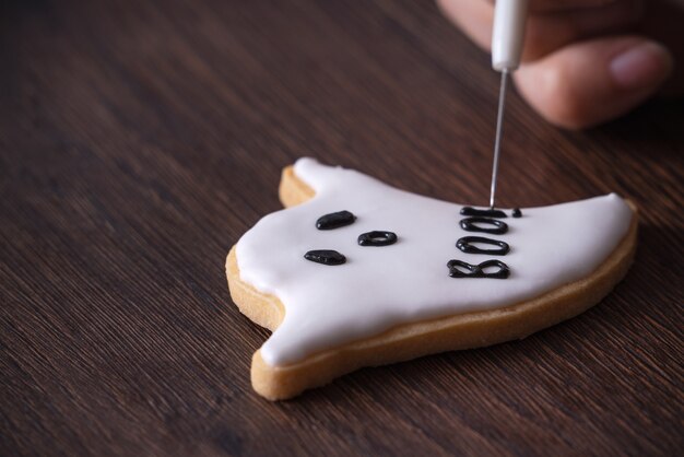 Photo close up of decorating cute halloween ghost gingerbread cookies with frosting icing cream topping bag.