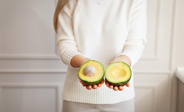 Close-up delicious avocado with stone in woman hands on light background. Healthy fresh food