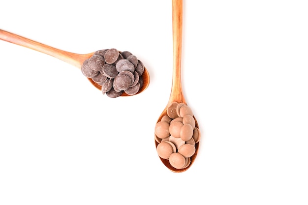 Close up of delicious dark and milk chocolate drops in wooden spoon isolated on white background Top view