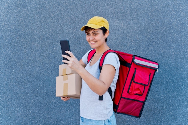 Close up of delivery woman with smartphone delivering parcel box . Technology and courier service concept. Horizontal view of rider delivering home a package.