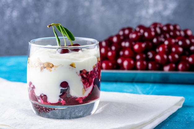 Close up dessert with cream and cherry in glass on cloth white napkin on blue grey background. berry dessert concept