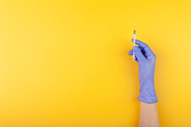 Close up doctor hand in medical glove holding syringe on yellow background