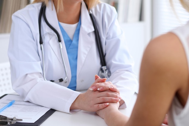 Close up of doctor hands reassuring her female patient. Medicine, help and health care concept