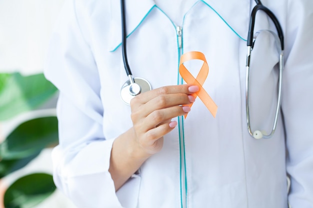 Close up of a doctor holding and showing orange awareness ribbon in her hands