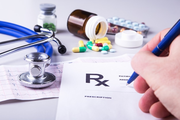 Close-up of doctor's hands writing prescription and holding bottle with pills.