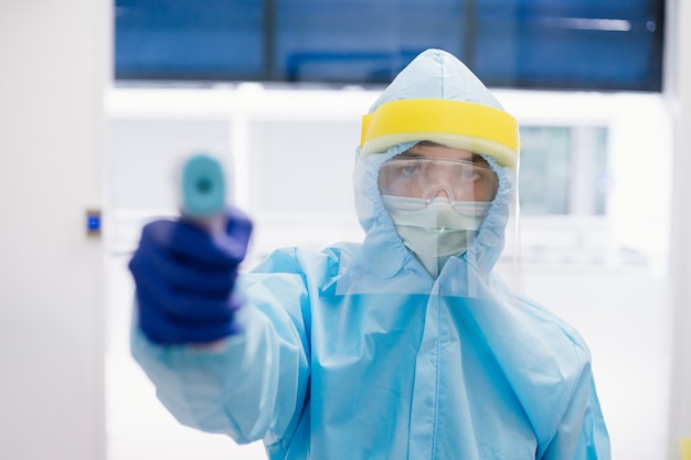 Close up of doctor wearing PPE suit uniform ready to use thermometer gun to check body temperature