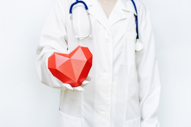 Close up on doctor in white coat and gloves holding red heart shape