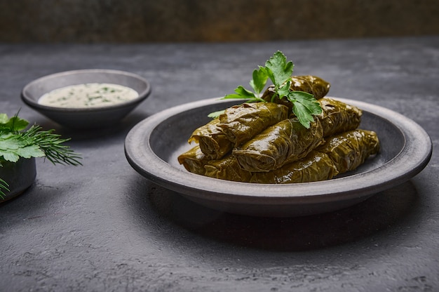 Close up dolma with sour cream on ceramic color graphite plate on dark table