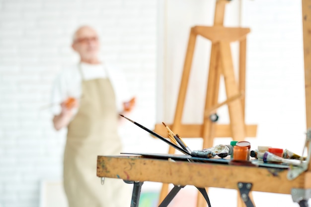 Close up of drawing instruments and tools, artist watercolors brushes and easel with male artist 