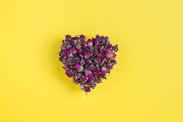 Close-up on dried pink  roses in the form of a heart on the yellow background. Copy space.