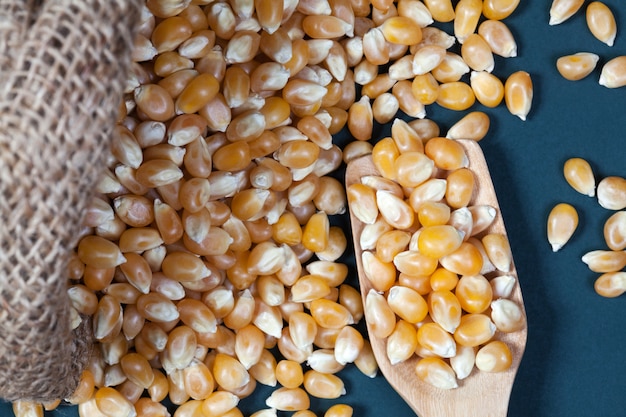 Close up dry corn kernels on a wooden spoon with the corn kernels are poured out from the hemp sack, photographing the top view.