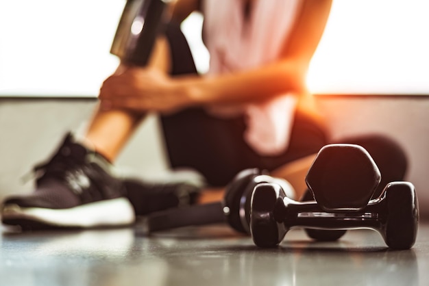 Photo close-up of dumbbell with woman sitting on floor in gym