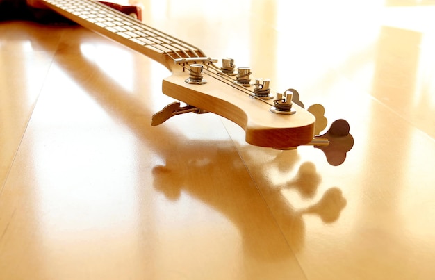 Close up of electric bass guitar, headstock with turning pegs of musical instrument on wooden floor