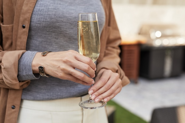 Close up of elegant woman holding champagne flute while standing at outdoor terrace during party, 