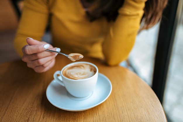 Close-up of elegant woman holding spoon to stir hot coffee.