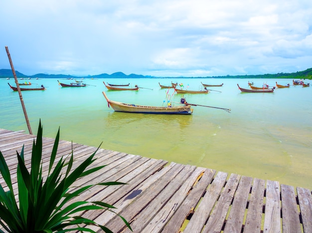 Close up empty wooden pier with local fisherman boats on the sea and sky background in Thailand.