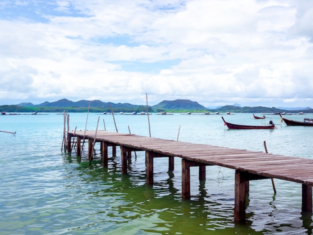 Close up empty wooden pier with local fisherman boats on the sea and sky background in Thailand.