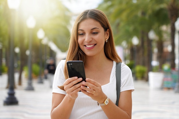 Close up of excited young woman watching her smartphone when walking in the street Millennial girl using mobile app outdoors Teenager lifestyle technology concept