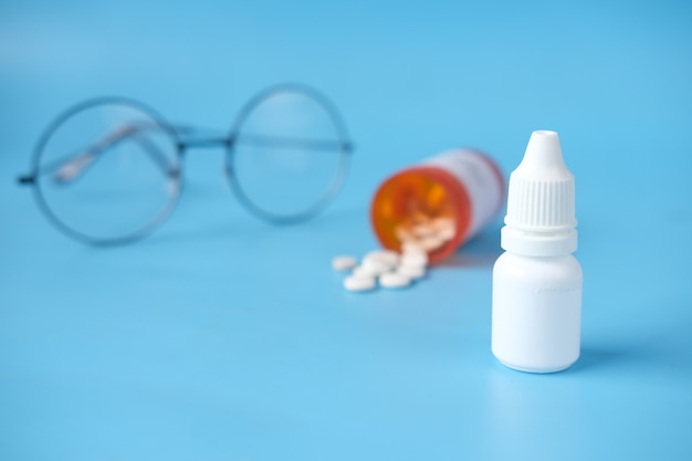 Close up of eye drop bottle and eyeglass on blue background