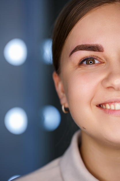 A close-up of the face of a young woman who has just had a permanent eyebrow tattoo done.