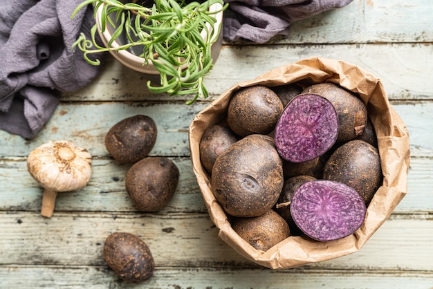 Close up of farm fresh purple potatoes in a paper bag on white wooden background top view