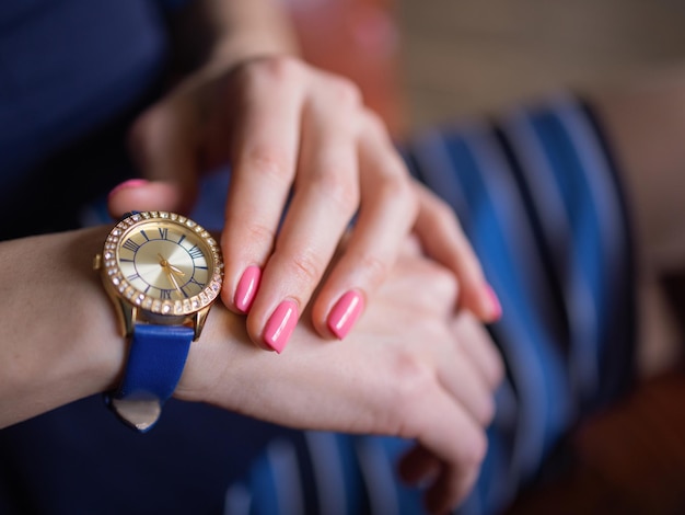 Close up fashion details, young business woman holding her golden watch. graded in warm colors.