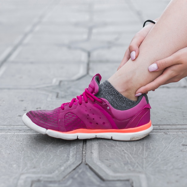 Close-up of female athlete having ankle pain on concrete pavement