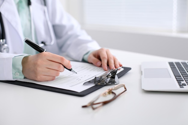 Close-up of a female doctor filling  out application form , sitting at the table in the hospital