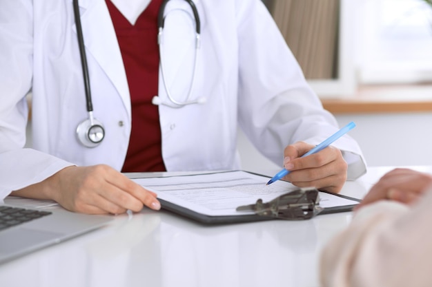 Close up of a female doctor filling up  an application form while consulting patient. Medicine and health care concept