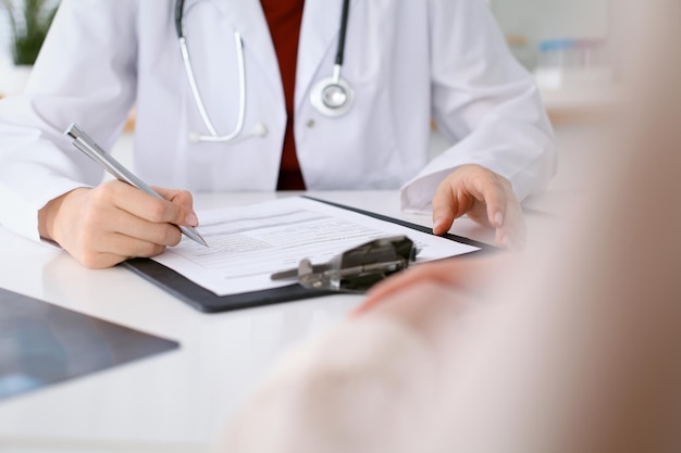 Close up of a female doctor filling up  an application form while consulting patient. Medicine and health care concept