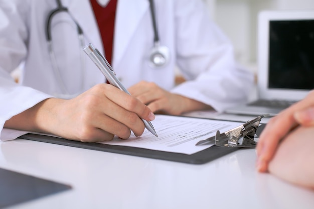 Close up of a female doctor filling up an application form while consulting patient