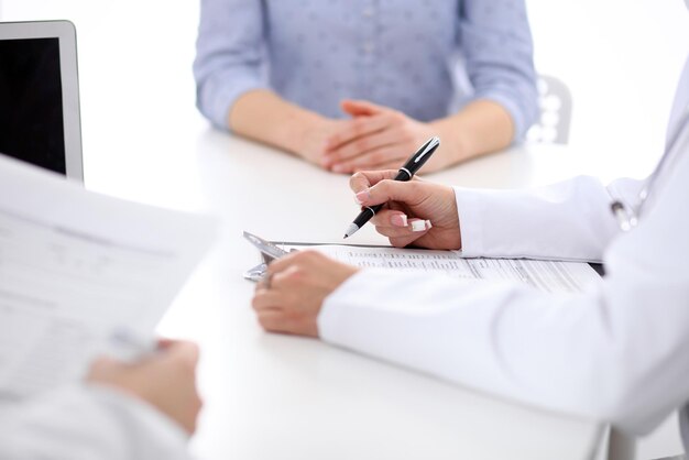 Close-up of a female doctor holding application form while consulting patient.