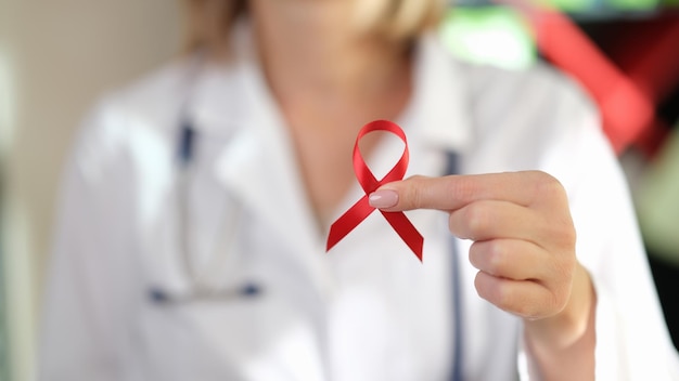 Close up of female doctor holds red ribbon in her hand as symbol of international aids day hiv