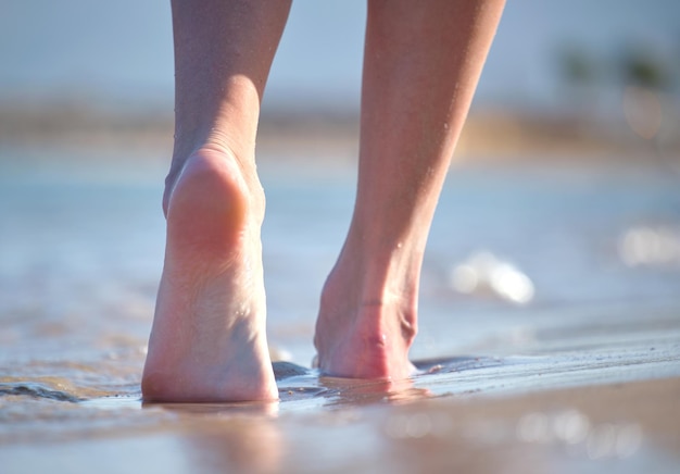 Close up of female feet walking barefoot on white grainy sand of golden beach on blue ocean water background