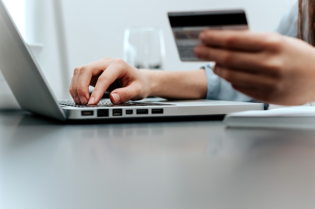 Close-up of female hand holding credit card and laptop making Internet purchase.