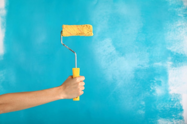 close up of female hand holding paint yellow roller over blue backgroundrepair