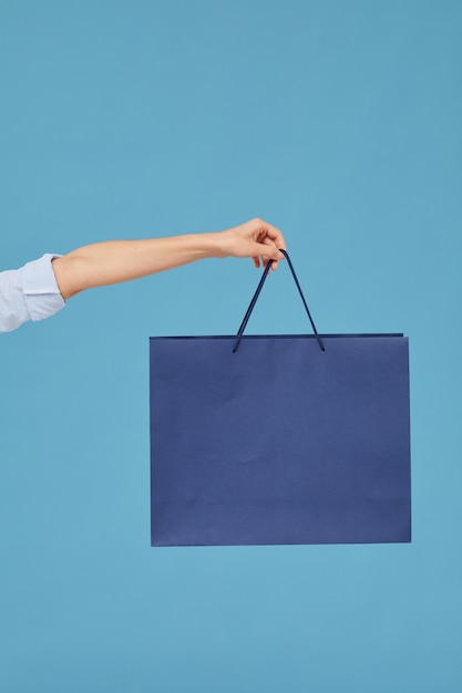 Close-up of female hand holding paper bag isolated on blue background