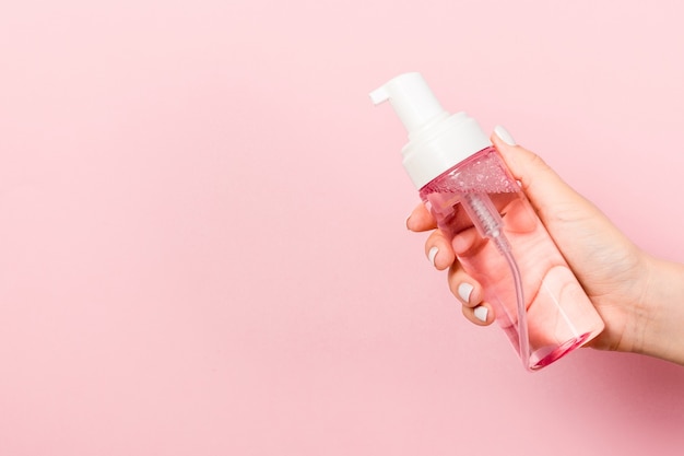 Close up of female hand holding a spray of cosmetics product at pink background with copy space.