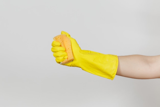 Close up of female hand in yellow gloves holds and squeezes yellow-orange sponge for cleaning and washing dishes isolated on white background. Cleaning supplies concept. Copy space for advertisement.