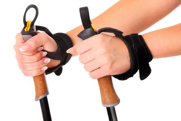 A close-up of female hands holding nordic walking sticks over white