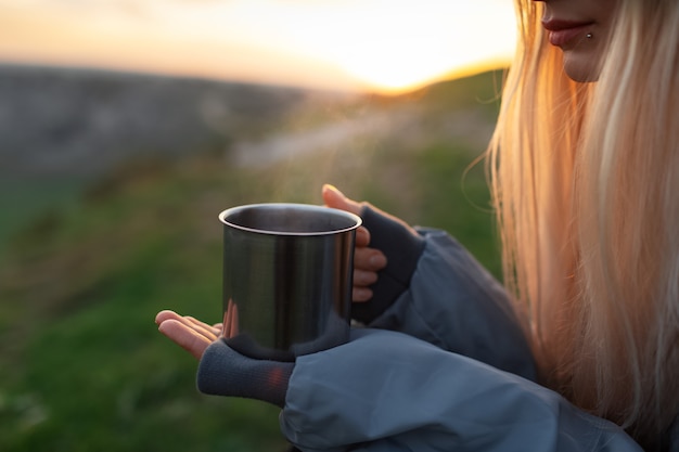 Close-up of female hands holding steel mug with hot tea outdoors