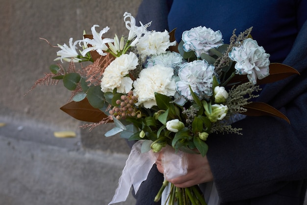 Close-up female hands holds white toned bouquet in vintage style outdoors on gray wall 