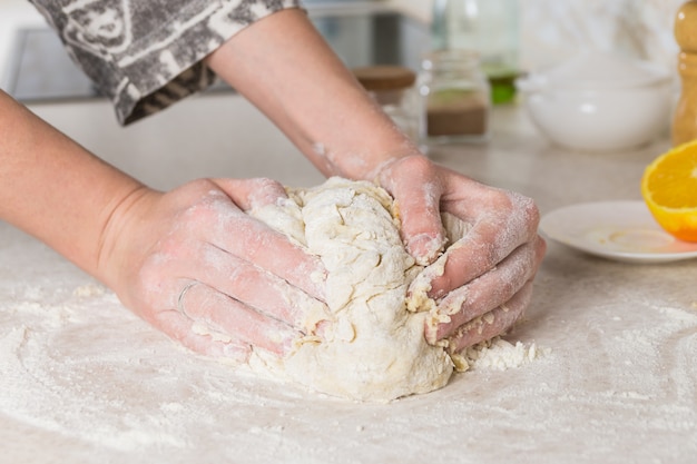 Close-up of female hands kneading dough in modern minimalistic kitchen. Preparing and mixing the dough.