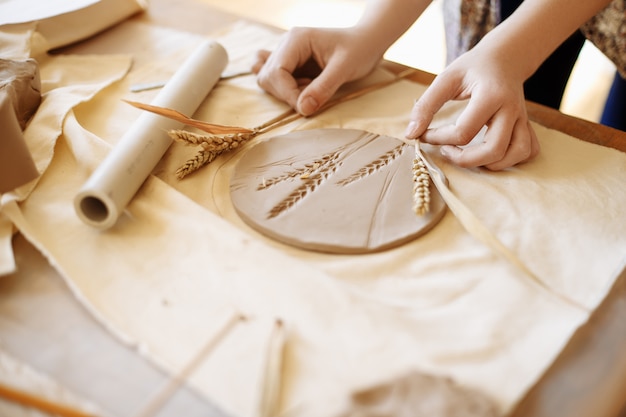 Close-up female hands make a clay plate, align the shape with special tools in the workshop