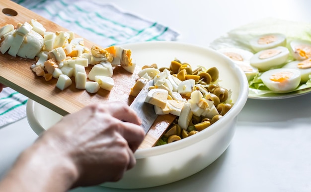 Close up of female hands slicing eggs on wooden board over a white table background