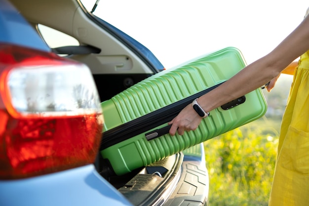 Close up of female hands taking green suitcase from car trunk. Travel and vacations concept.